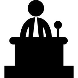 Businessman talking with a mic behind a table icon